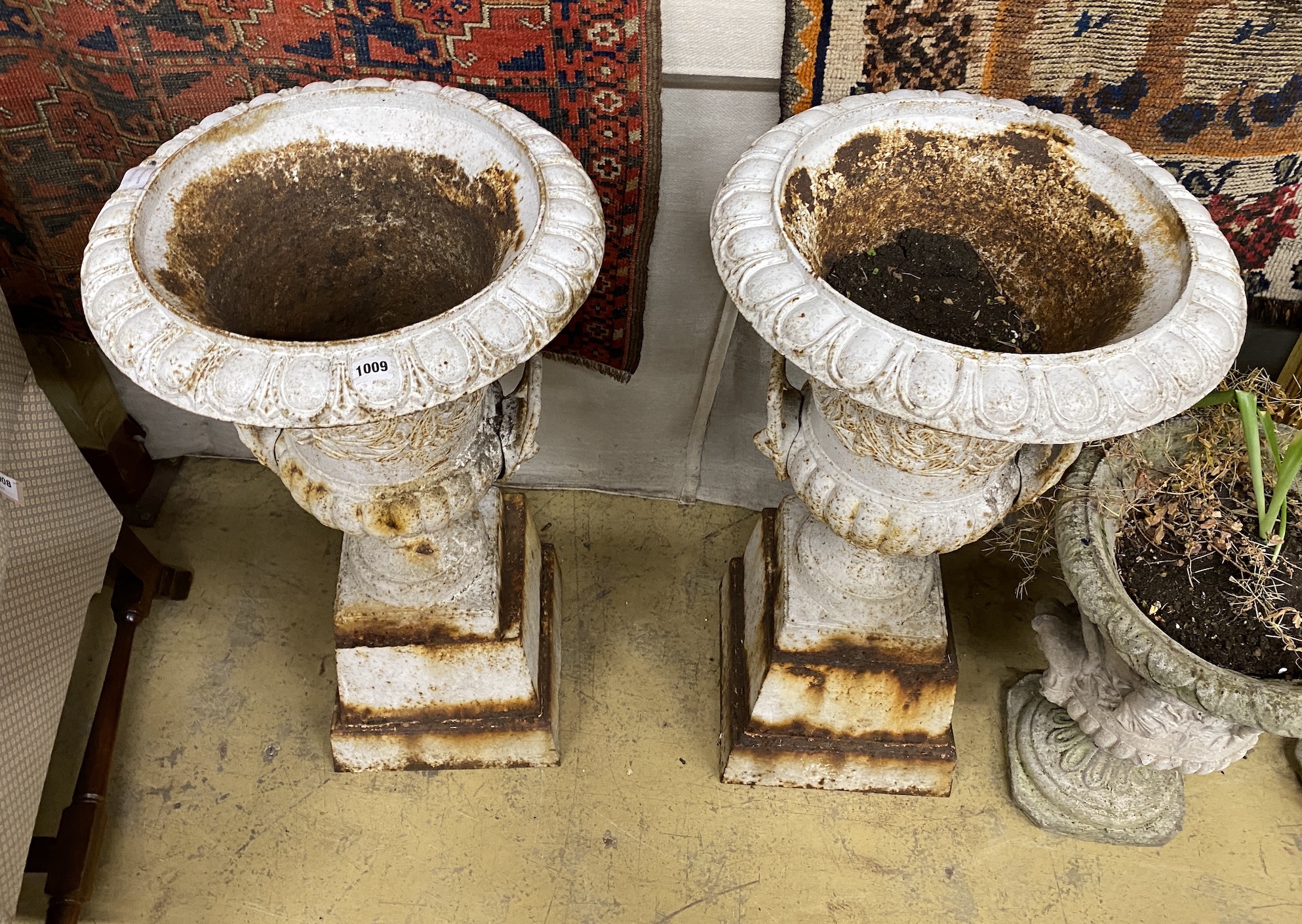 A pair of painted cast iron campana garden urns on stepped square plinths, diameter 46cm, height 90cm